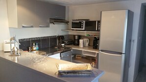 Een moderne keuken met een RVS spoelbak, een magnetron, een koffiezetapparaat en een koelkast.