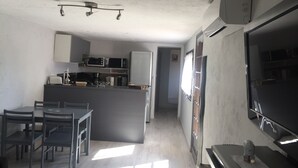 Een kleine keuken met een magnetron, broodrooster en koelkast. Er is een eethoek met een tafel en stoelen.