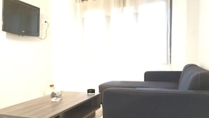 Een woonkamer met een donkere bank, een houten salontafel en een flatscreen televisie aan de muur.