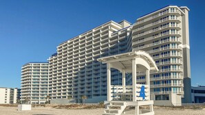 Un hotel frente a la playa con varios edificios altos, una torre de salvavidas y una playa de arena.