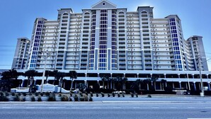 Un hotel de varios pisos con un atrio central, balcones y un área de estacionamiento al frente.