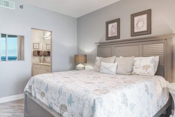 A bedroom with a large bed, a vanity with a mirror, and framed artwork on the wall. - Direct Gulf Front ~ Oversized Balcony ~ 3BR 3BA ~ 7th Floor ~ GulfShoresByOwner (Gulf Shores)