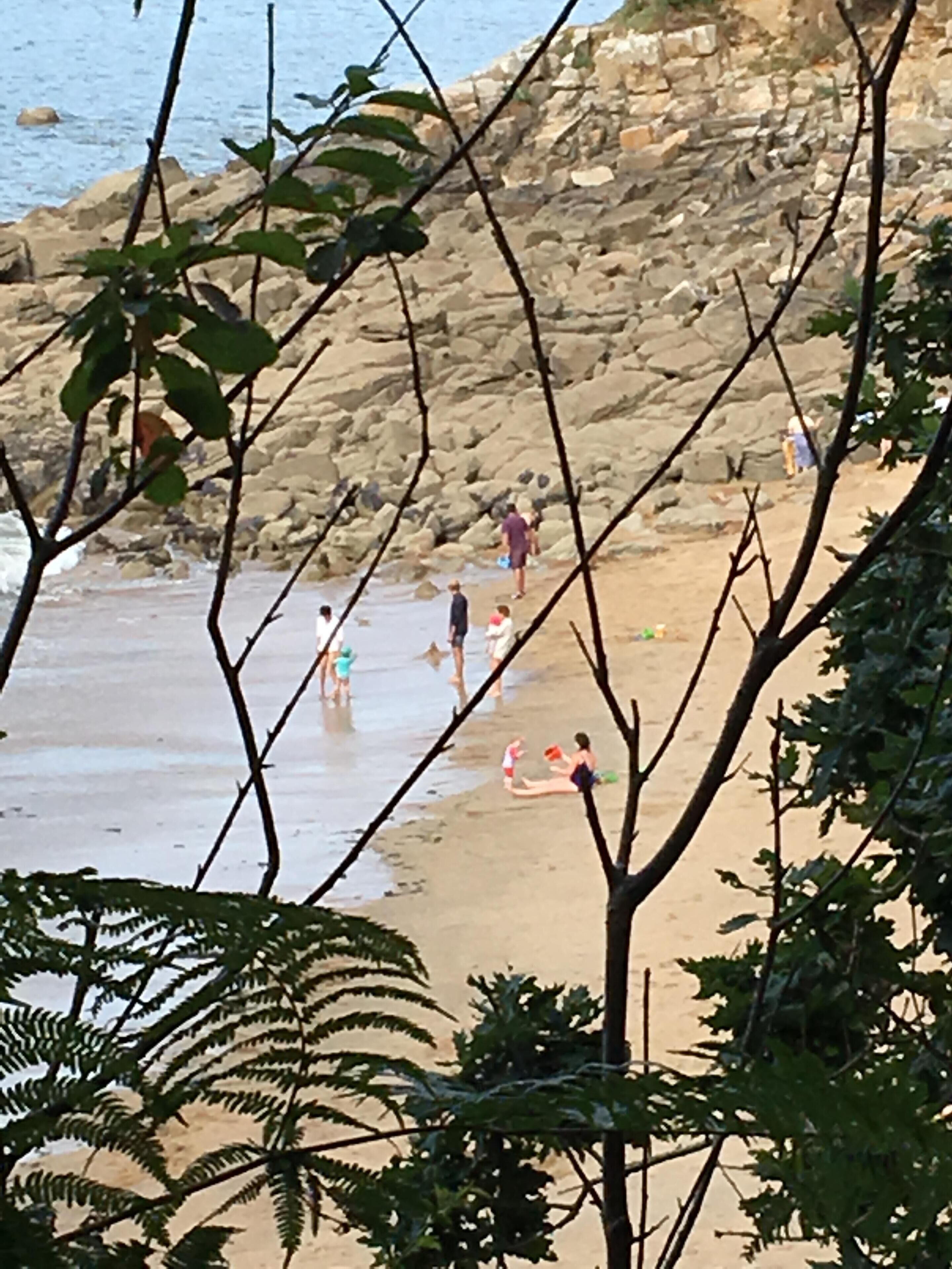 Una playa con terreno rocoso y gente realizando diversas actividades.