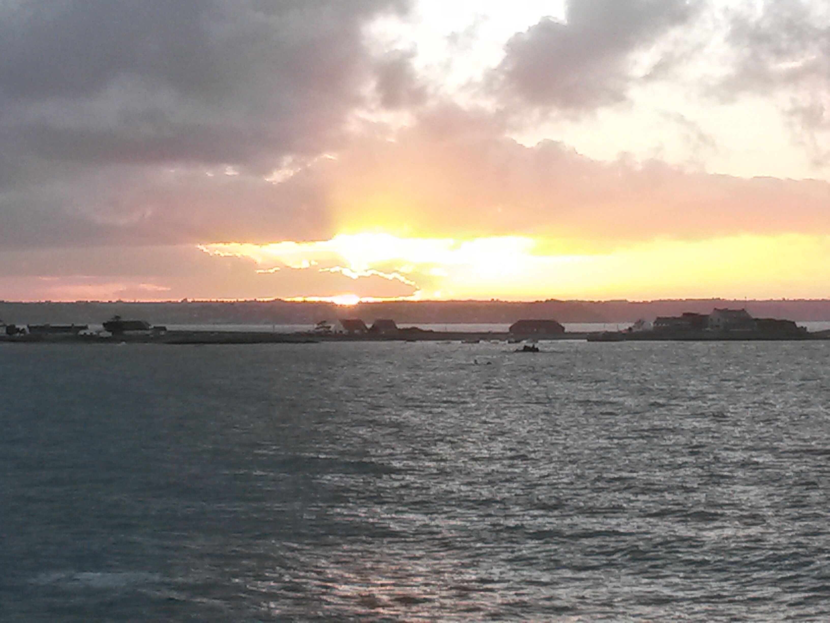 A sunset over a body of water with a distant shoreline and buildings.