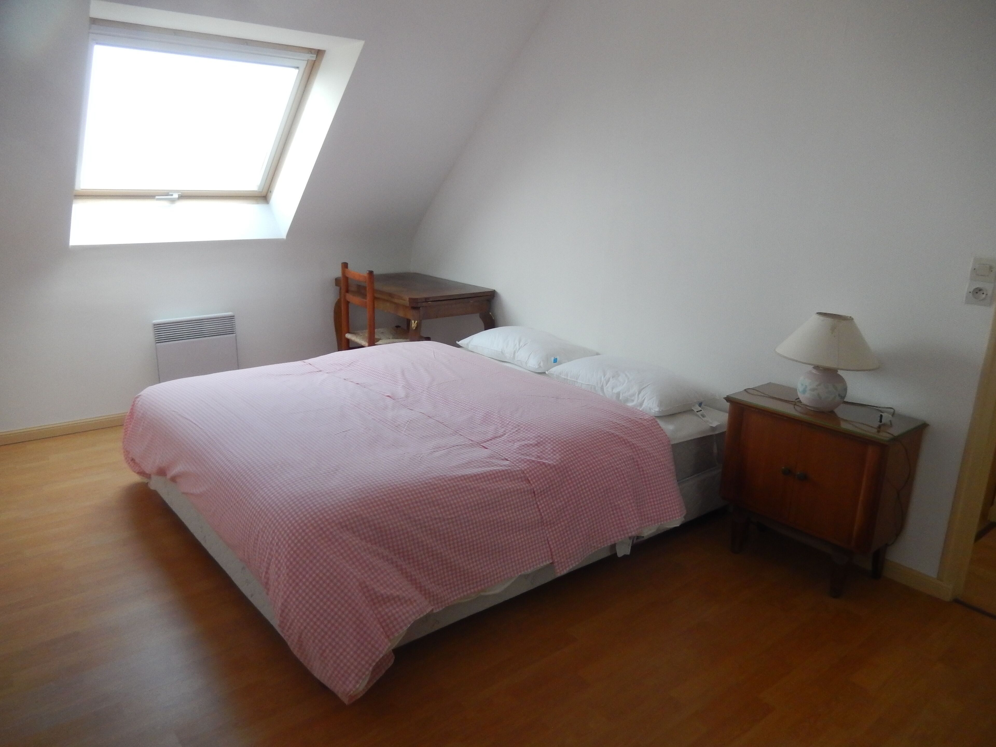 A bedroom with a single bed, a wooden nightstand, a desk, and a window.