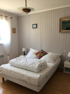 Una cama bien hecha con ropa blanca, un cojín de lunares coloridos y un pequeño cuadro en la pared.