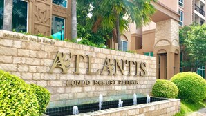 Exterior del Atlantis Condo Resort Pataya, con un muro de piedra, un elemento acuático y jardines bien cuidados.