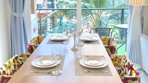 Comedor con una mesa preparada para cuatro personas, una araña y vistas a un paisaje urbano y zonas verdes.
