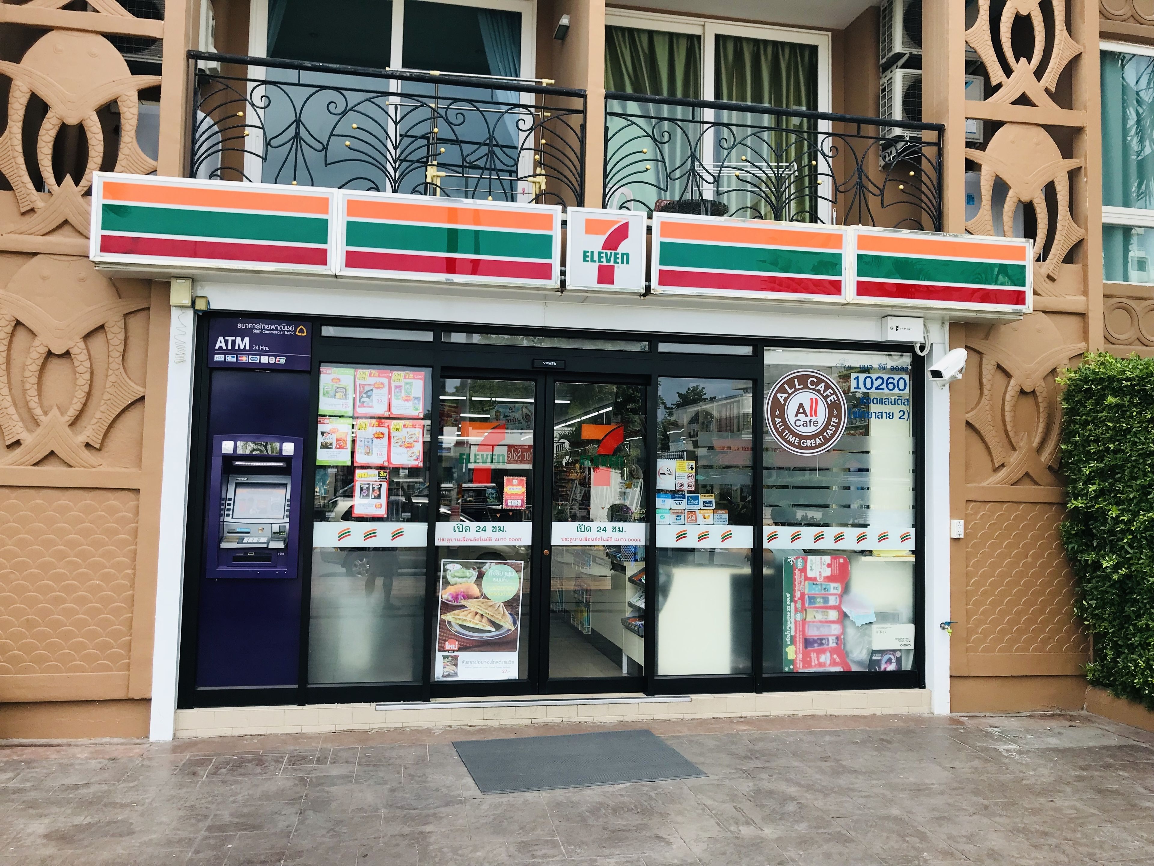 Ein 7-Eleven-Kiosk mit Geldautomat, verschiedenen Werbeanzeigen für Lebensmittel und einer Überwachungskamera.