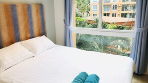 Habitación de hotel con cama, ropa de cama blanca, cabecero a rayas y vistas a edificios y zonas verdes por la ventana.