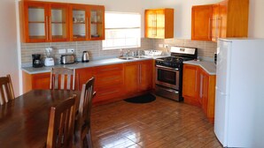 Une cuisine avec des meubles de rangement en bois, une cuisinière, un réfrigérateur et une table à manger avec des chaises.