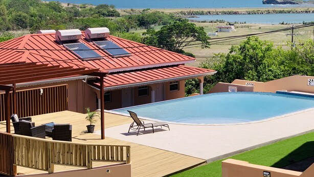 Une piscine avec vue sur l’océan, un patio couvert avec des sièges et des panneaux solaires sur le toit.