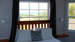 Une chambre à coucher avec une tête de lit en bois, un lit avec une literie blanche et un oreiller à motifs, une table de chevet avec une télécommande et une fenêtre avec des rideaux.