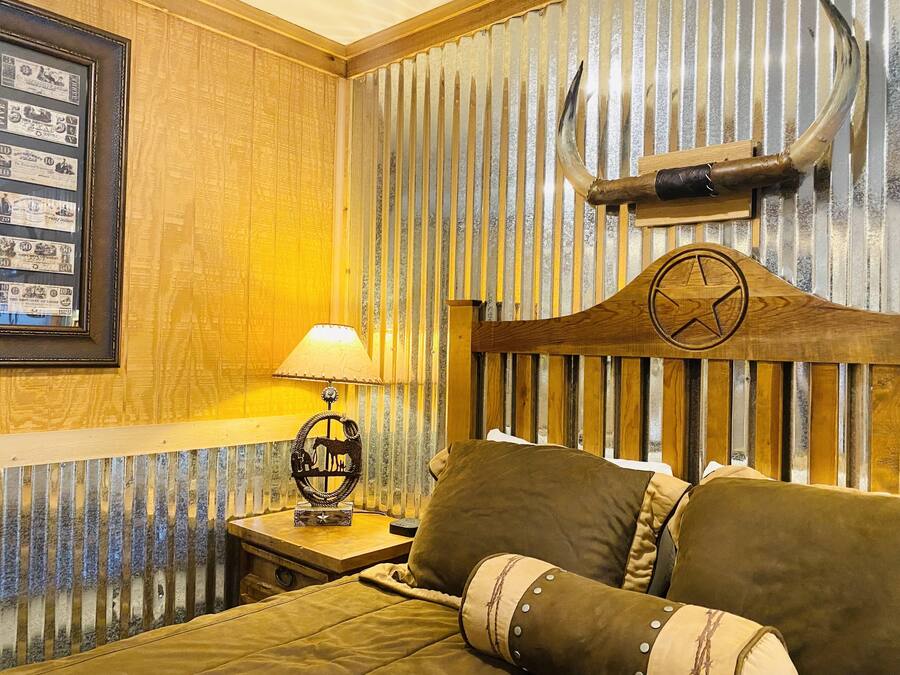 Una habitación con cabecera de madera, un cuadro en la pared, una lámpara sobre una mesita auxiliar y una cama con almohadas.