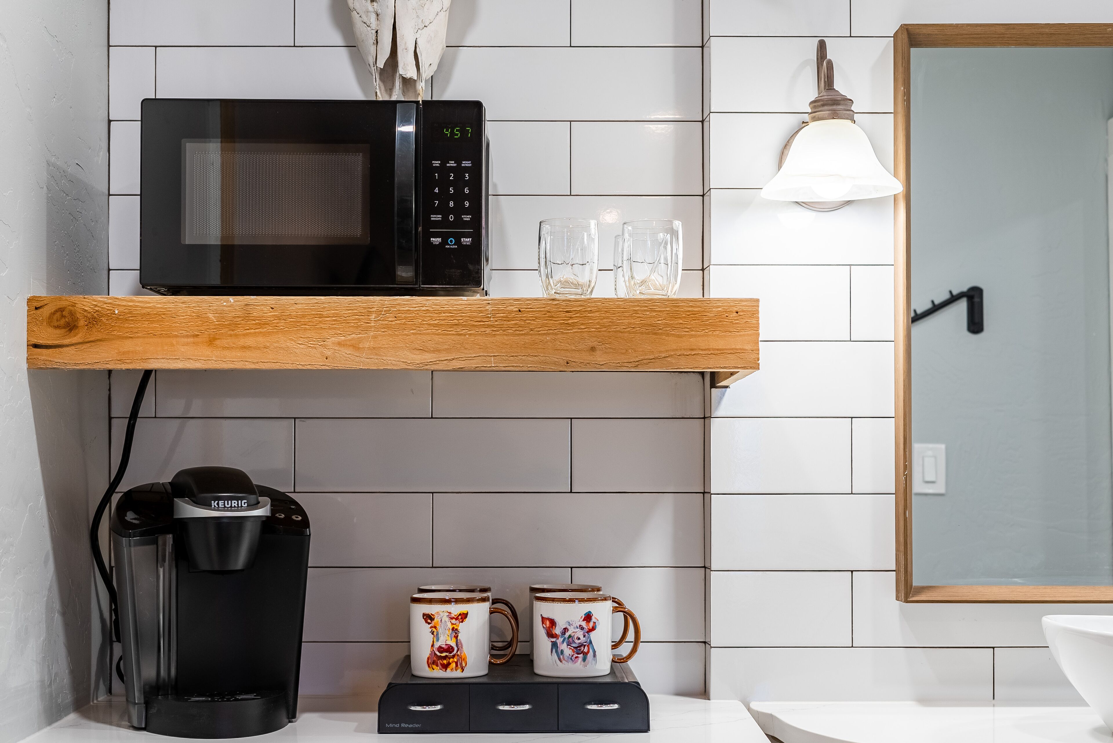 A kitchen area with a microwave, coffee maker, and two mugs on a shelf.