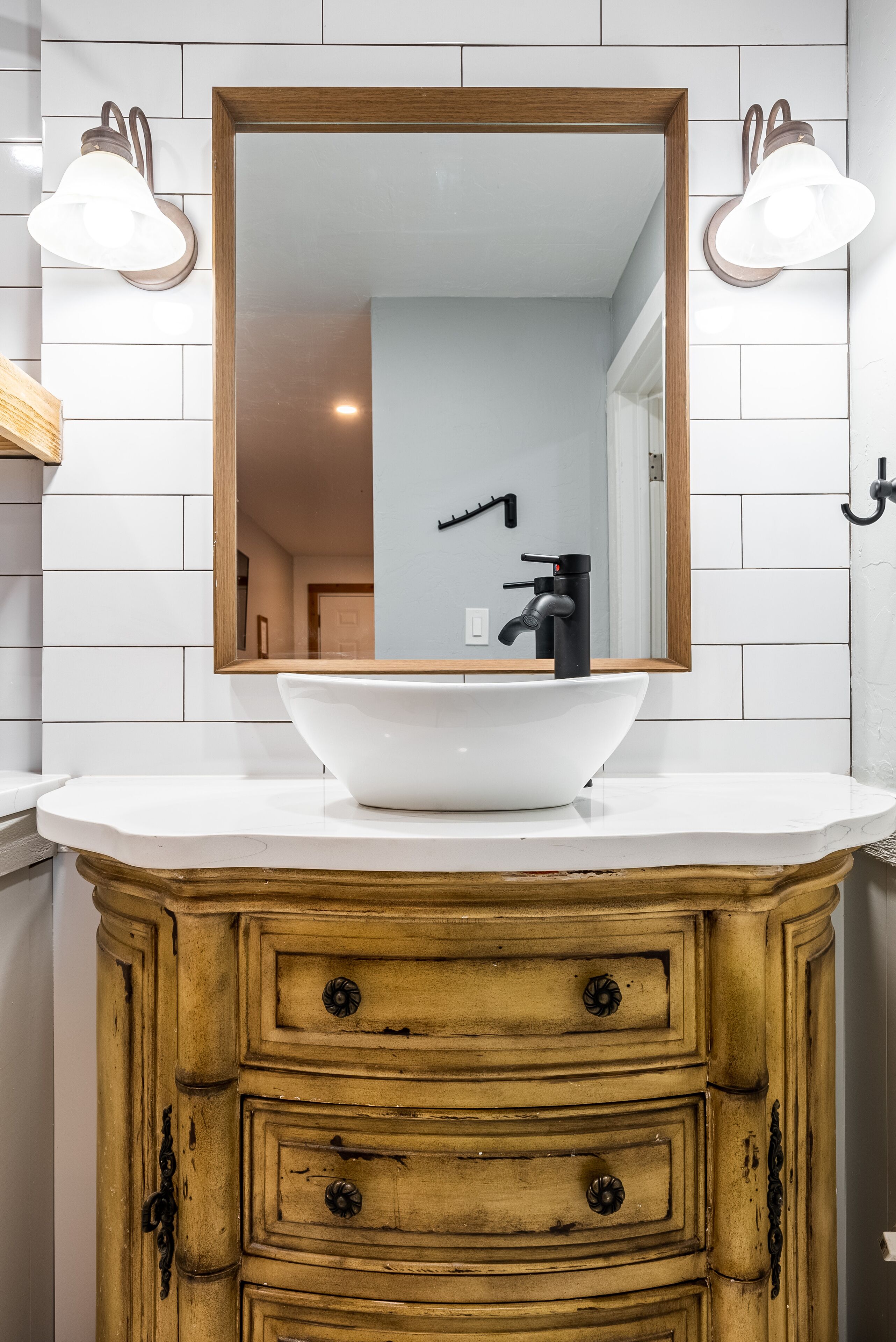 Un baño con lavamanos blanco, tocador de madera y un espejo con dos luces empotradas.