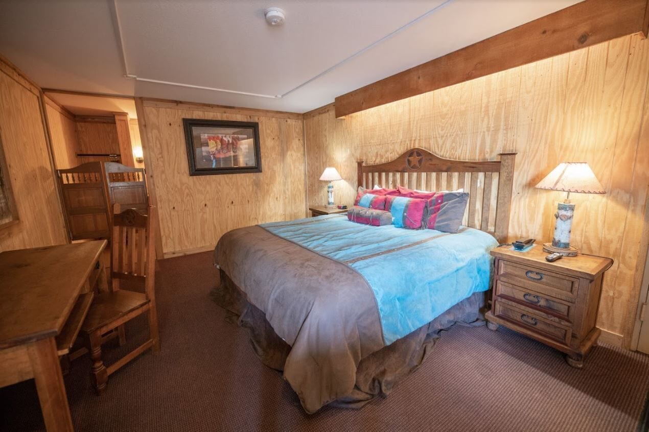A wooden-themed bedroom with a bed, bedside tables, a desk, and a chair.