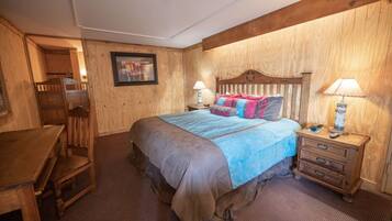 A wooden-themed bedroom with a bed, bedside tables, a desk, and a chair.