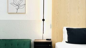 A hotel room with a green sofa, a bed with white bedding, a bedside table with a lamp, and a wooden panel wall.