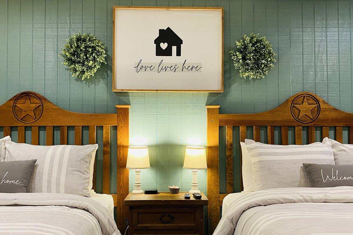 A bedroom with two beds, a nightstand with lamps, and a framed sign above the beds.