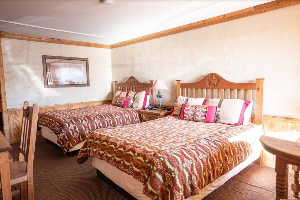 A hotel room with two single beds, wooden headboards, and a small table.