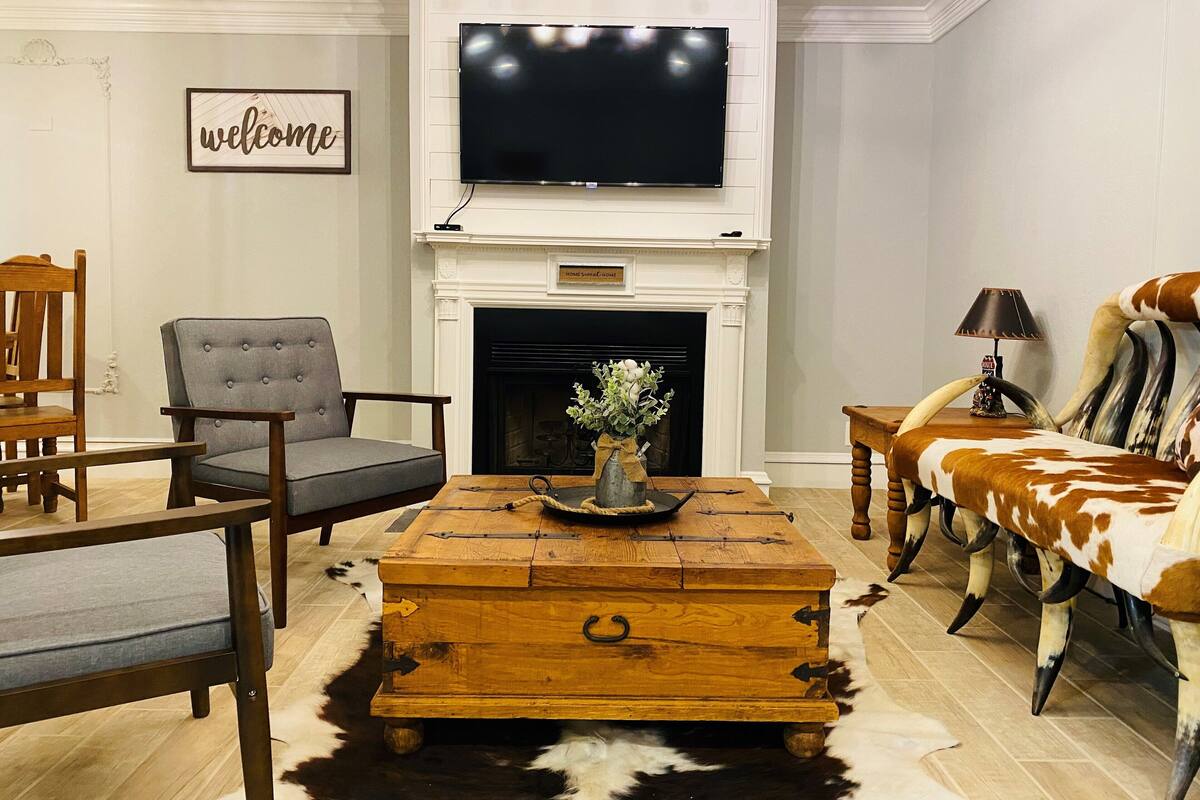 A living room with a fireplace, a television mounted above it, a wooden coffee table, and a cowhide rug.