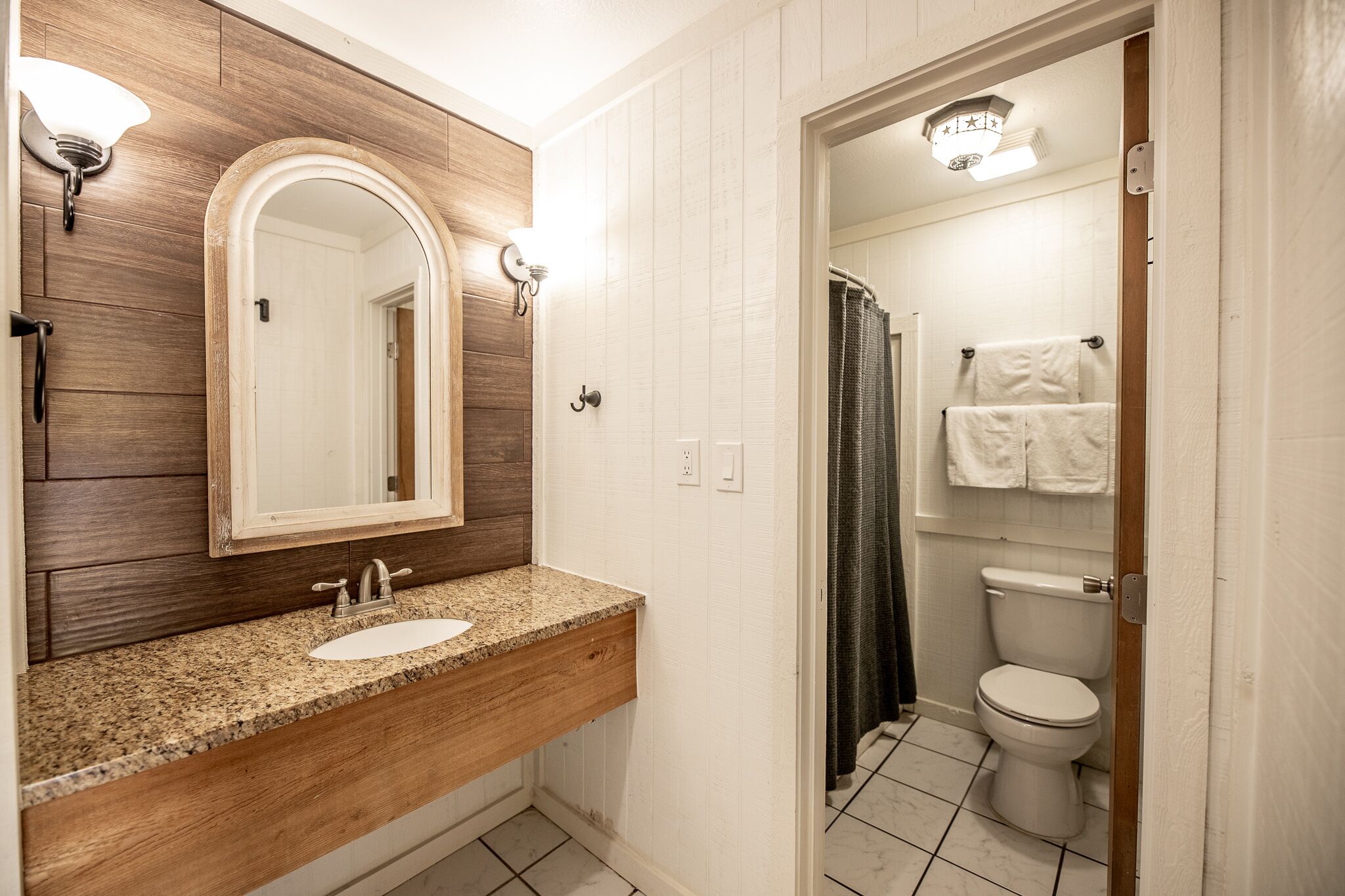 Un baño con tocador de madera, lavamanos, espejo e inodoro.