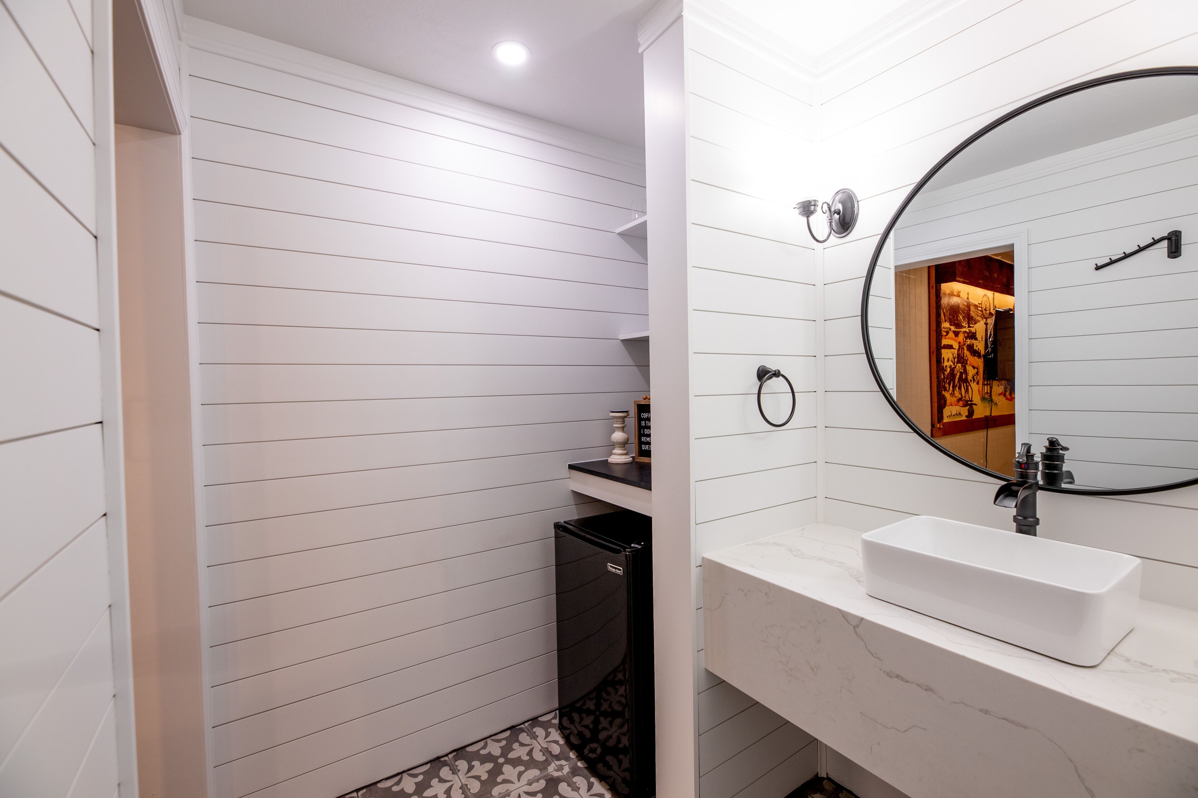 A modern bathroom with a white vanity, a rectangular sink, a round mirror, and a small trash bin.