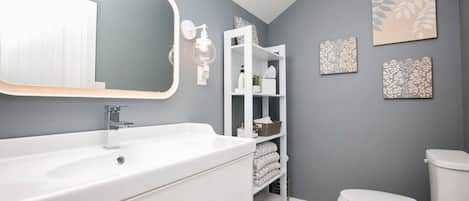 A modern bathroom with a white sink, a toilet, and a shelf with towels.