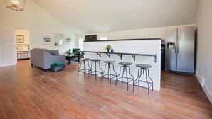Una cocina moderna con barra, un sofá gris y un refrigerador de acero inoxidable.
