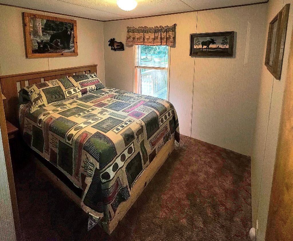 Ein Schlafzimmer mit einem hölzernen Bett, einer gesteppten Decke, einem Fenster mit Vorhängen und Wanddekorationen, darunter gerahmte Bilder.