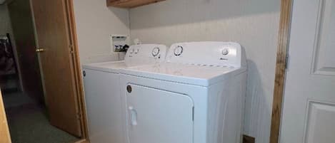 A compact laundry room with a front-loading washer and dryer, wooden cabinets above, and a fire extinguisher on the wall.
