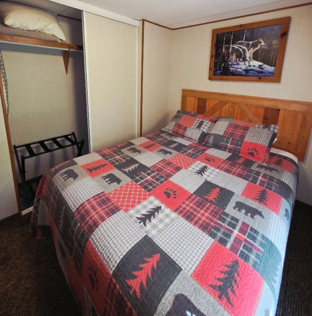Un dormitorio con cama, cabecera de madera, un cuadro colgado en la pared, armario y una silla metálica.