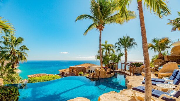 Ein Poolbereich eines Resorts mit klarem, blauem Wasser, Palmen und Blick auf den Ozean.