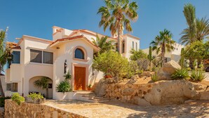 Eine mediterran gestaltete Villa mit Steinverkleidung, einer Holztür und einer Steintreppe, die zum Eingang führt.