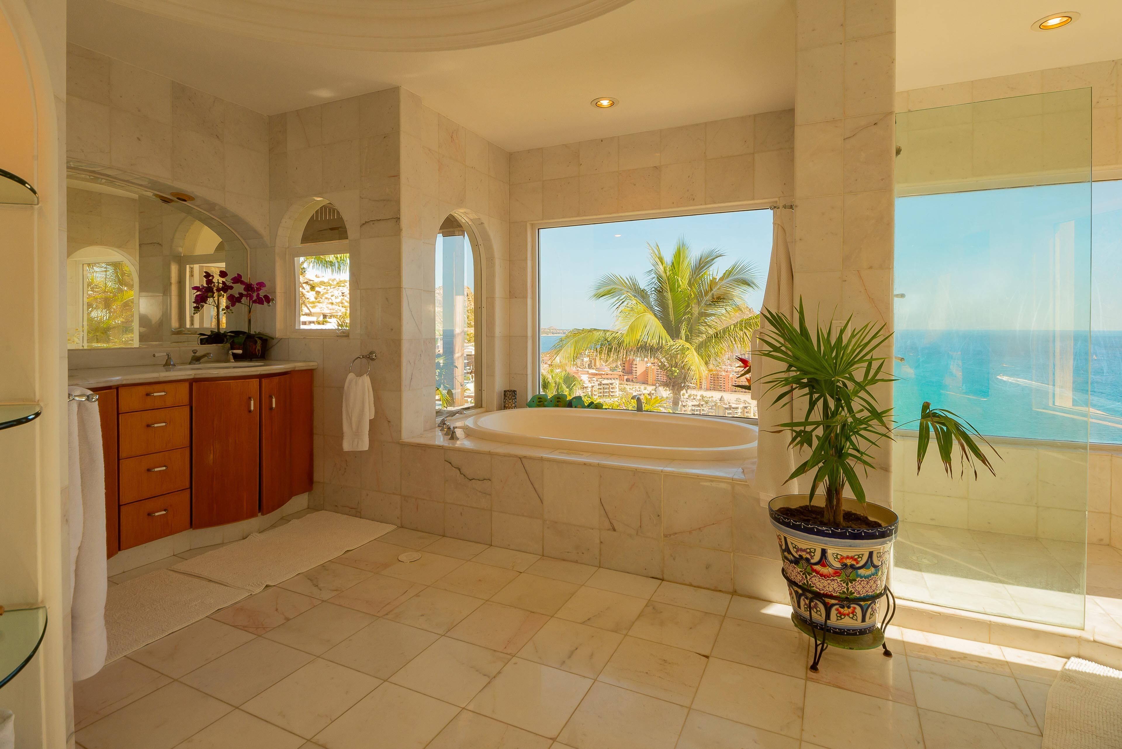 Un baño amplio con una bañera grande, un tocador con espejo y una planta en maceta.
