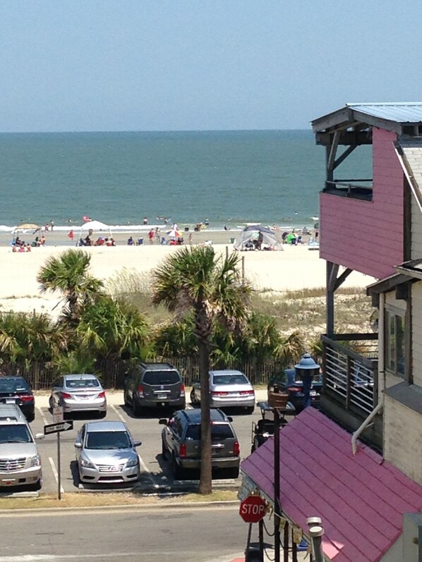 A beach view with parked cars, a stop sign, and a building with a pink roof.