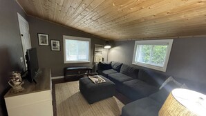A cozy living room with a wooden ceiling, a dark gray sofa, a white side table, and a lamp. - Our Cozy Getaway  (Ocean Park)
