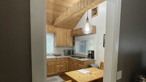 A compact kitchen with wooden cabinets, a dining table, and a hanging light fixture. - Our Cozy Getaway  (Ocean Park)