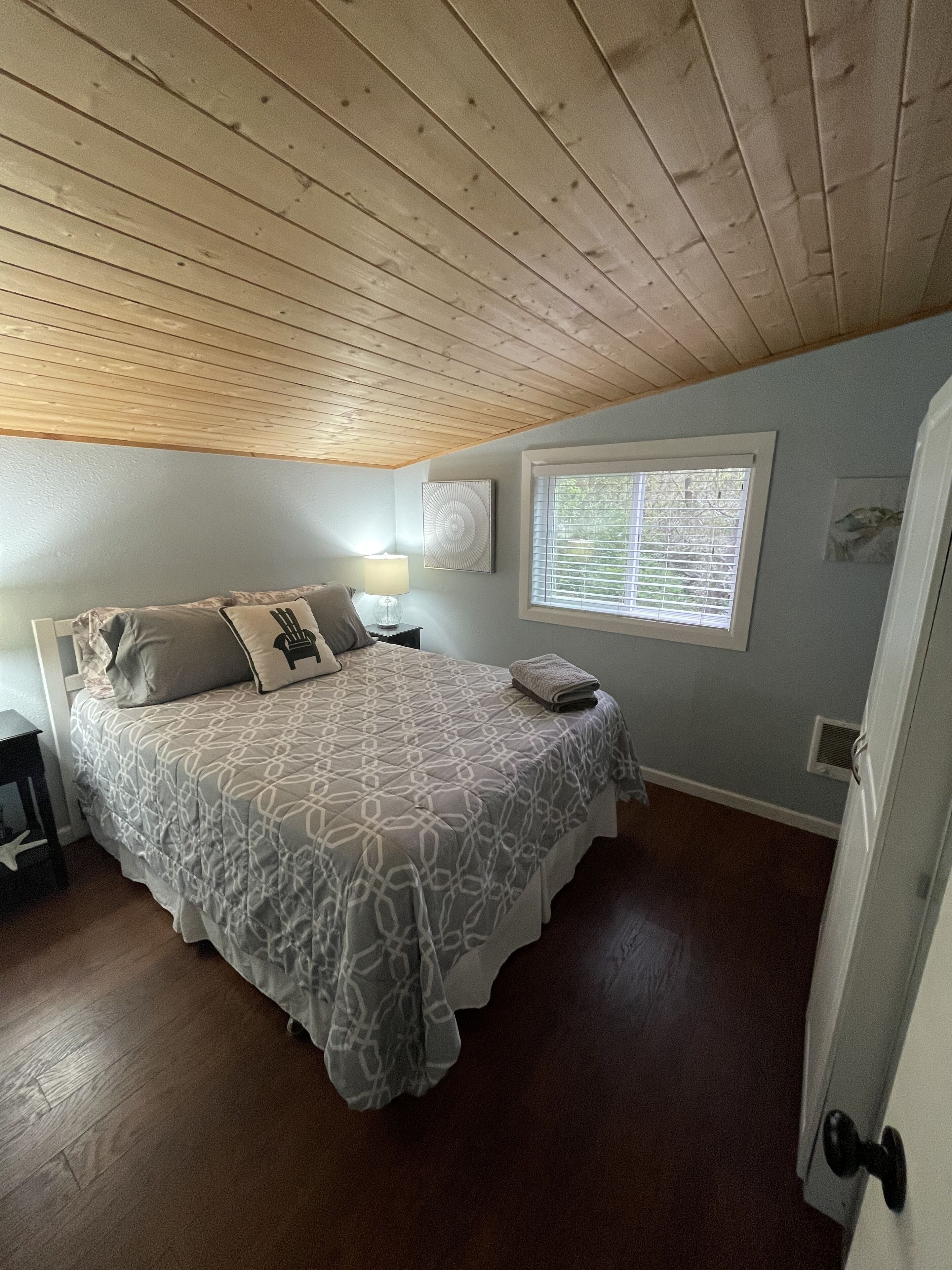 A bedroom with a bed, a nightstand, a lamp, a window, and a door.