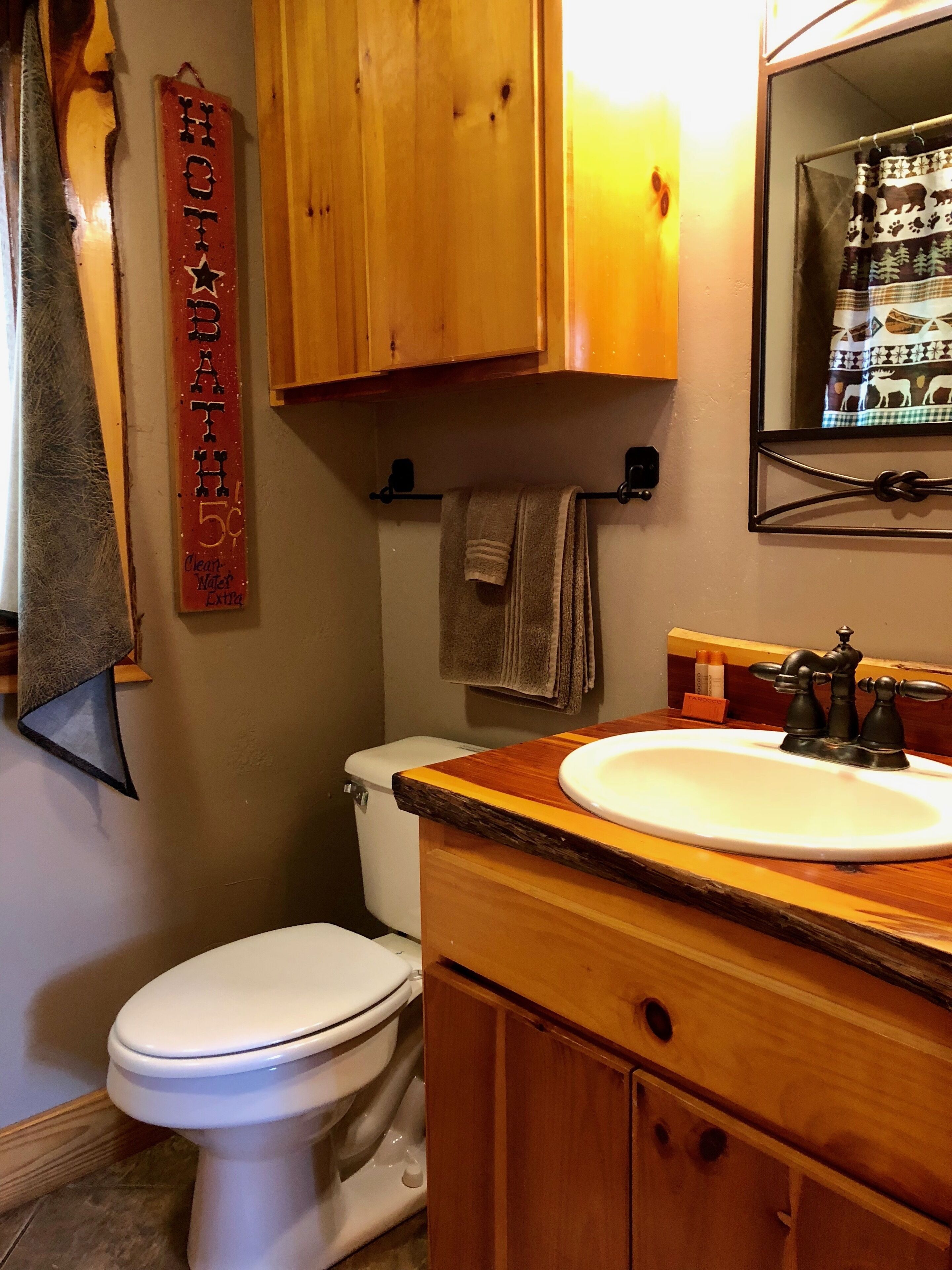 Een badkamer met een wit toilet, houten kastjes, een wastafel met een vintage kraan en een handdoekhouder.