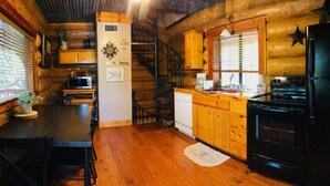 L’intérieur d’une cabane en bois comprend une cuisine, un coin repas et un escalier.
