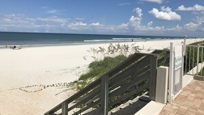 Ein Strand mit einer Holztreppe, die zum Sand führt, einem Schild mit der Aufschrift 'Seawall nicht betreten' und einem strahlend blauen Himmel.