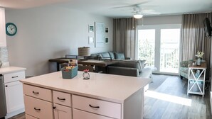 Eine moderne Küche mit einer zentralen Kochinsel, ein Essbereich mit einer Couch und ein Balkon mit Vorhängen.