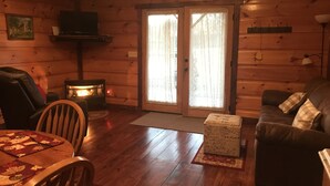 A cozy cabin interior with a fireplace, wooden walls, a sofa, and a dining table. - Private Catch & Release Lake - Boat Rental Included! Close To Lake Cumberland! (Russell Springs)