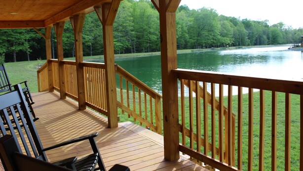 A wooden deck with a railing overlooking a lake, surrounded by trees. - Private Catch & Release Lake - Boat Rental Included! Close To Lake Cumberland! (Russell Springs)