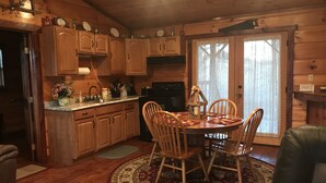 A wooden cabin interior with a dining area, wooden cabinets, a kitchen with appliances, and a large window. - Private Catch & Release Lake - Boat Rental Included! Close To Lake Cumberland! (Russell Springs)