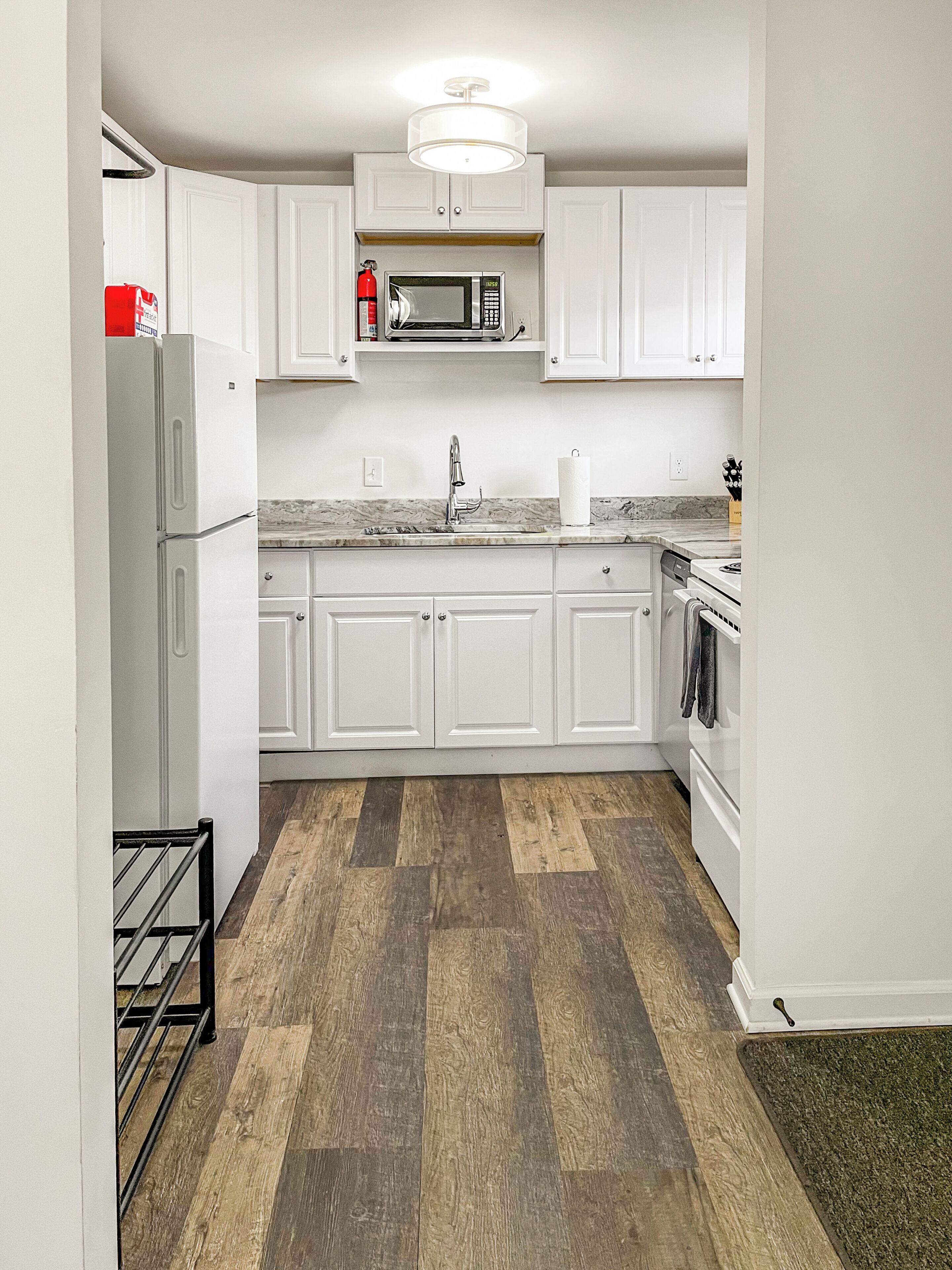 A kitchen with white cabinets, a stainless steel refrigerator, a microwave, a sink, and a stove.