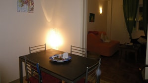 Ein Essbereich mit Tisch, Stühlen und einer Lampe. Im Hintergrund befindet sich eine Couch und ein Gemälde.