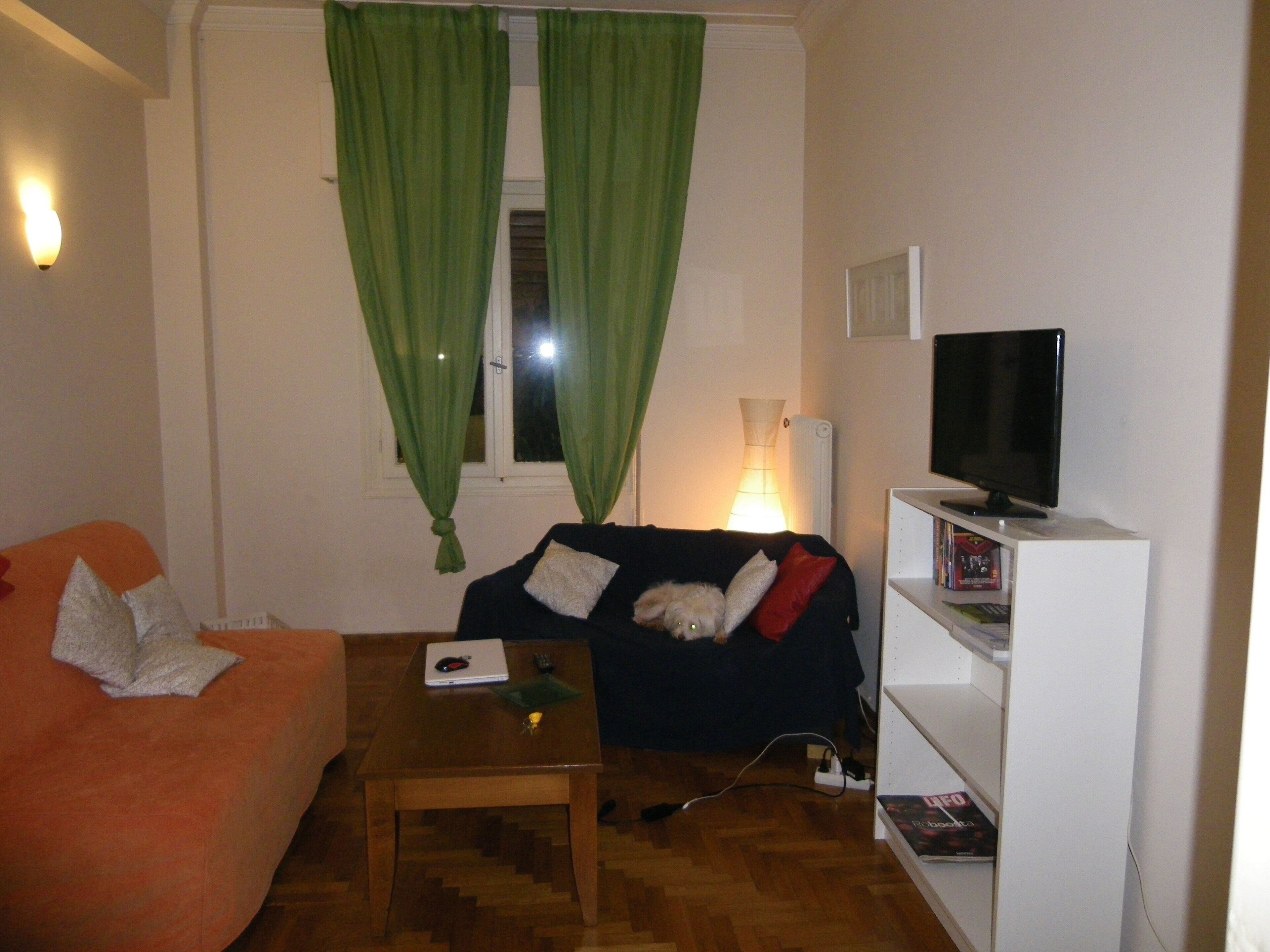 A living room with a sofa, a coffee table, a TV on a stand, and a bookshelf.